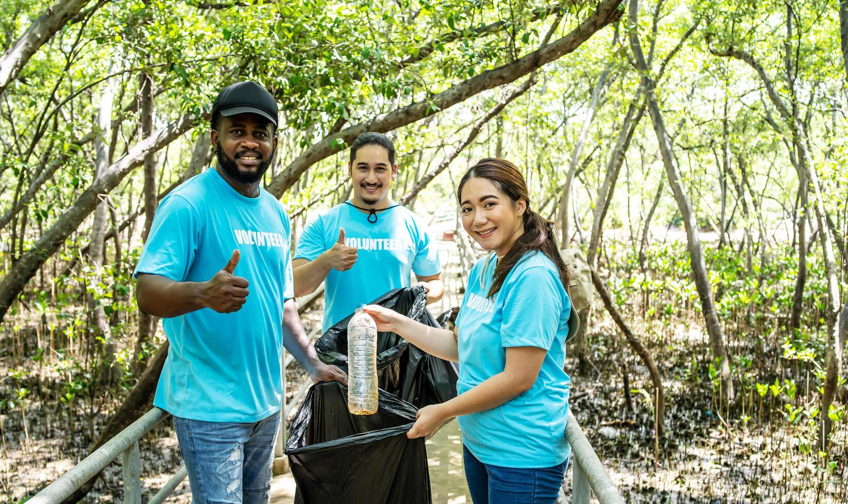 Three volunteers in work overalls collect garbage in forest in plastic bag. Close-up during action. Cleaning of nature from waste. Environmental assistance. Garbage collection in forest photo