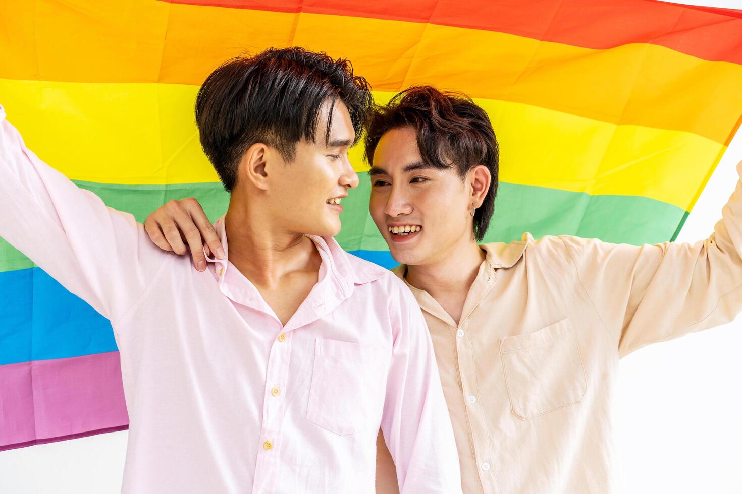 Portrait of Happy gay couple showing their love with rainbow flag. holding each other and holding up an LGBTQ flag, They are laughing, LGBT and love concept. photo