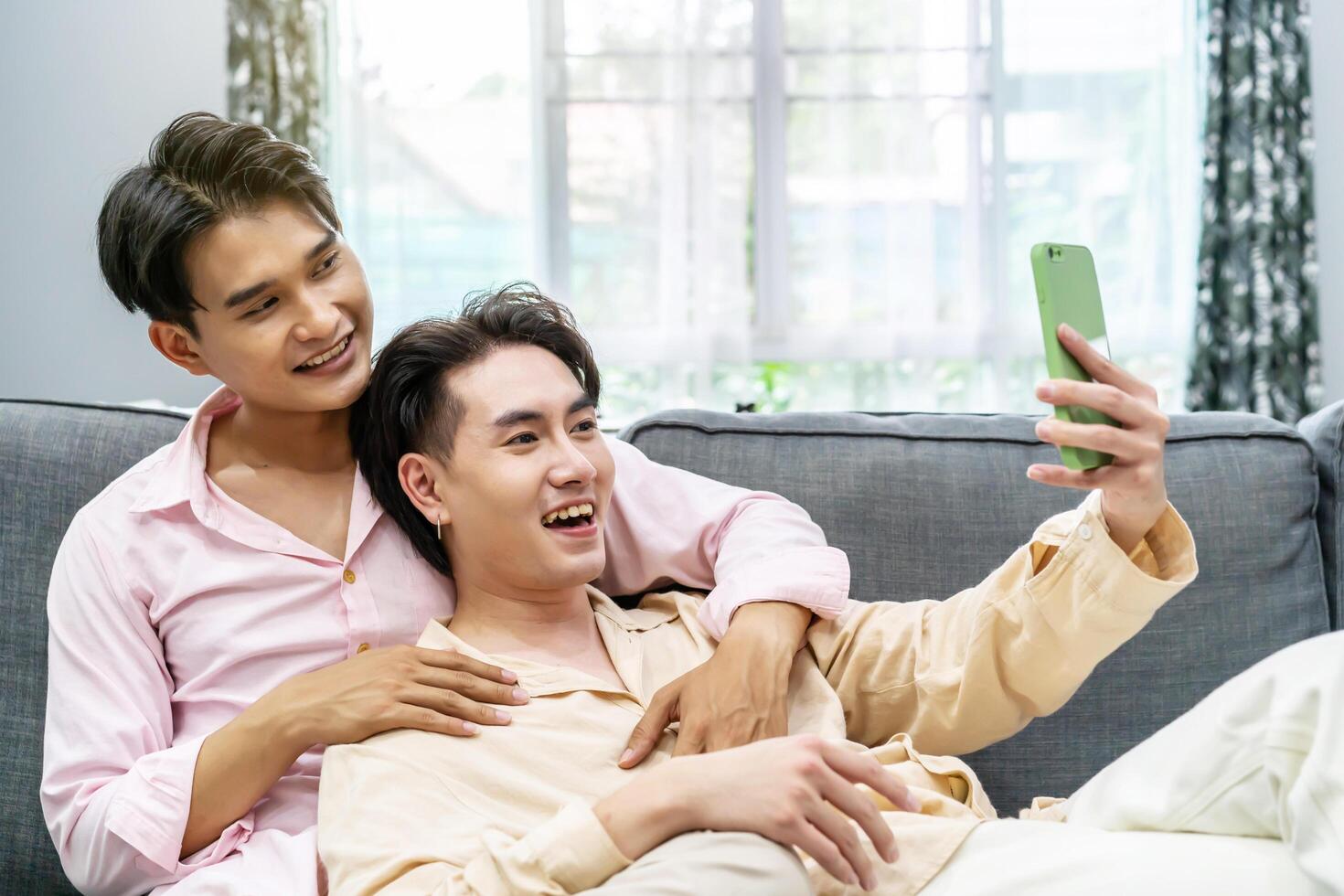 Guys Smile and Laugh in Love. Cute Male Homosexual Gay Couple Spend Time Together, Men Taking Selfie on Smartphone, sitting on a sofa in sitting room, LGBTQ, LGBT Pride Month, Gay Pride Symbol photo
