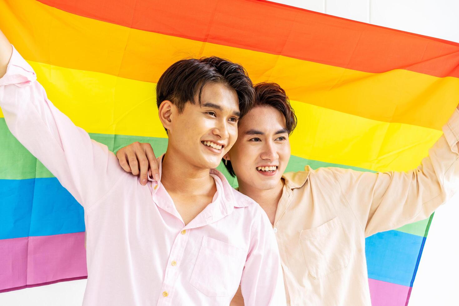 Portrait of Happy gay couple showing their love with rainbow flag. holding each other and holding up an LGBTQ flag, They are laughing, LGBT and love concept. photo