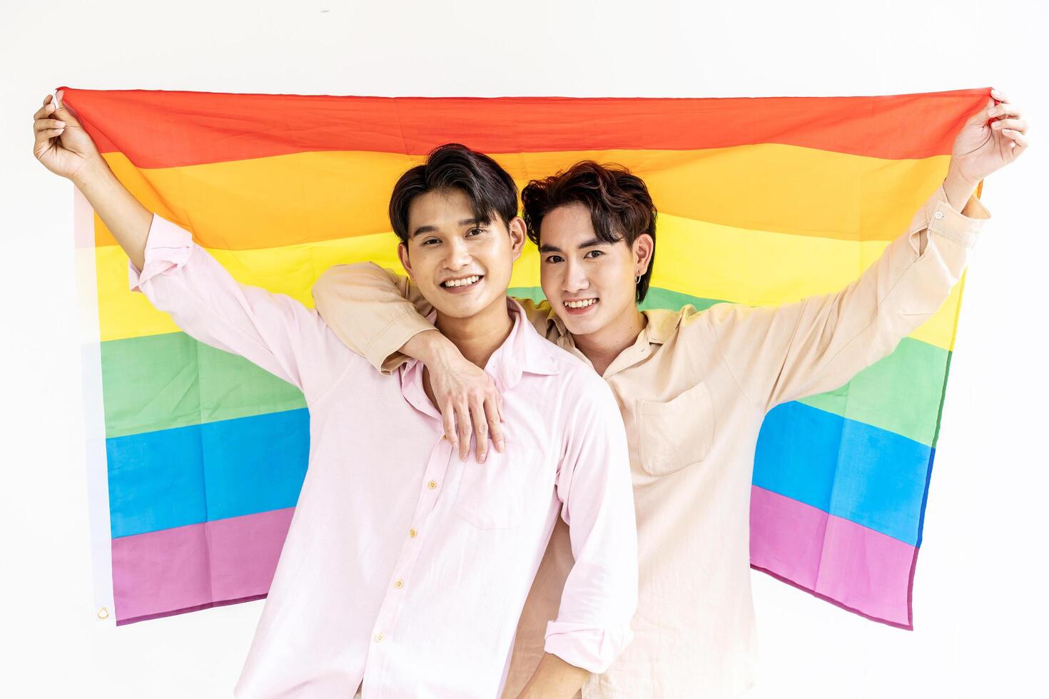 Portrait of Happy gay couple showing their love with rainbow flag. holding each other and holding up an LGBTQ flag, They are laughing, LGBT and love concept. photo