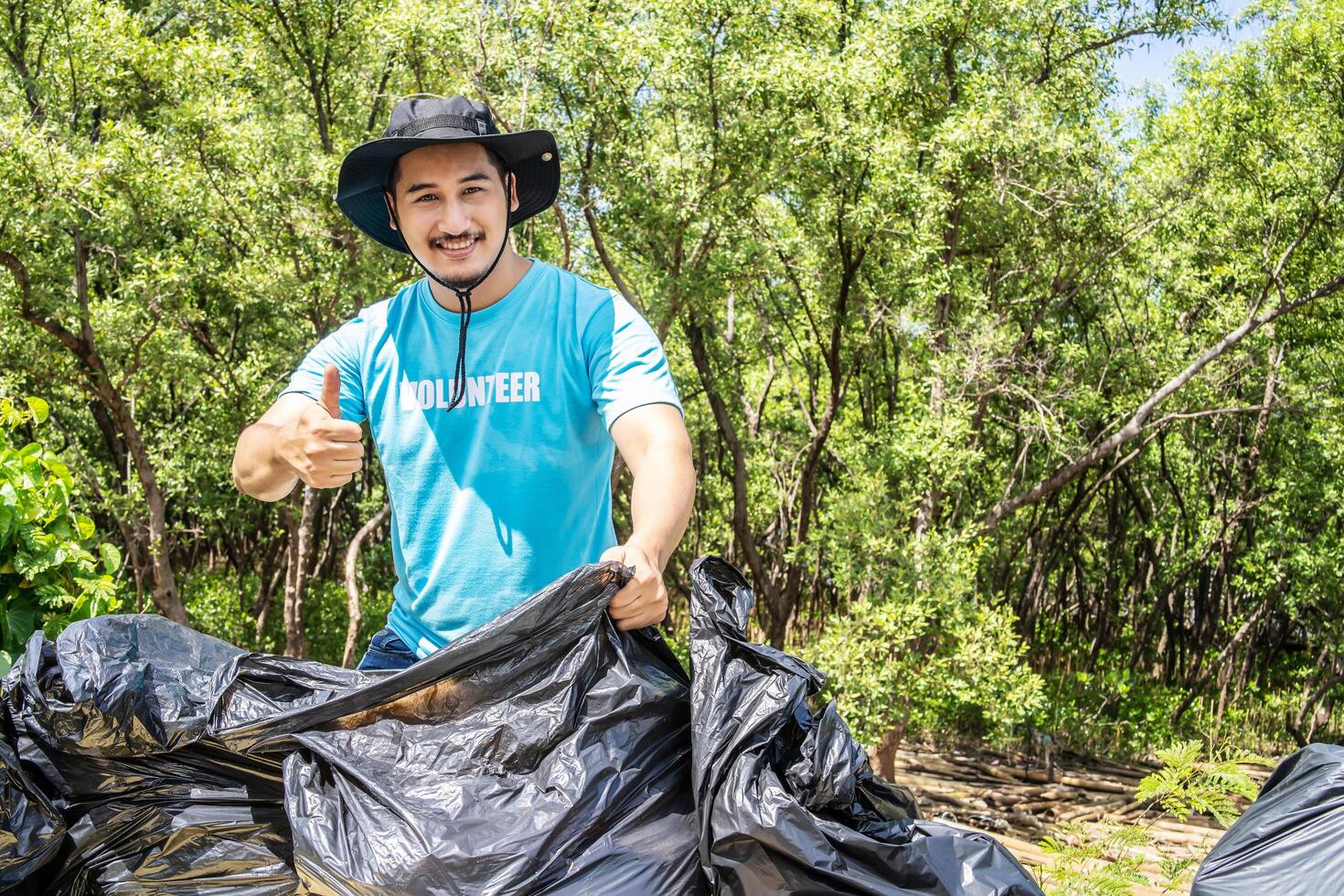 One volunteers in work overalls collect garbage in forest in plastic bag. Close-up during action. Cleaning of nature from waste. Environmental assistance. Garbage collection in forest photo