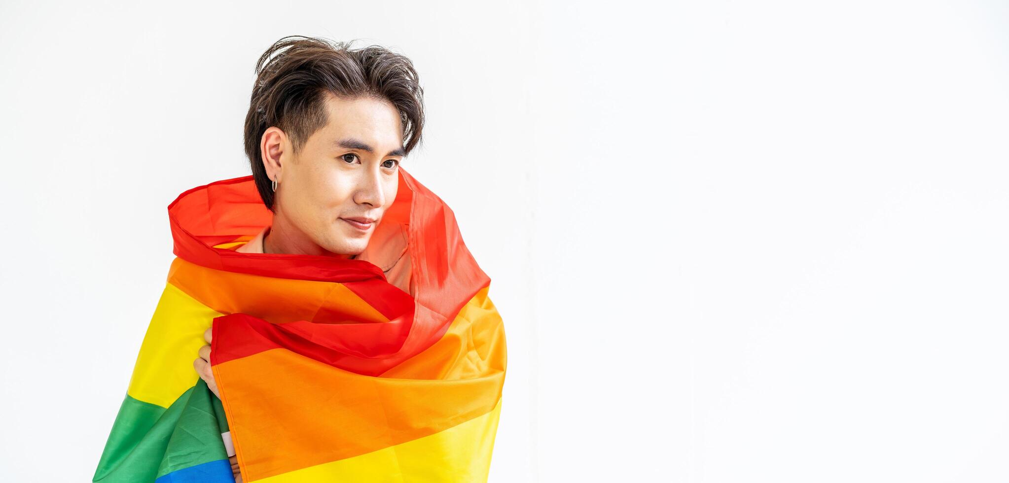 Portrait of transgender or gay man smiling in front of camera taking cover with lgbt flag on white background with copy space. People lifestyle fashion lgbtq concept photo