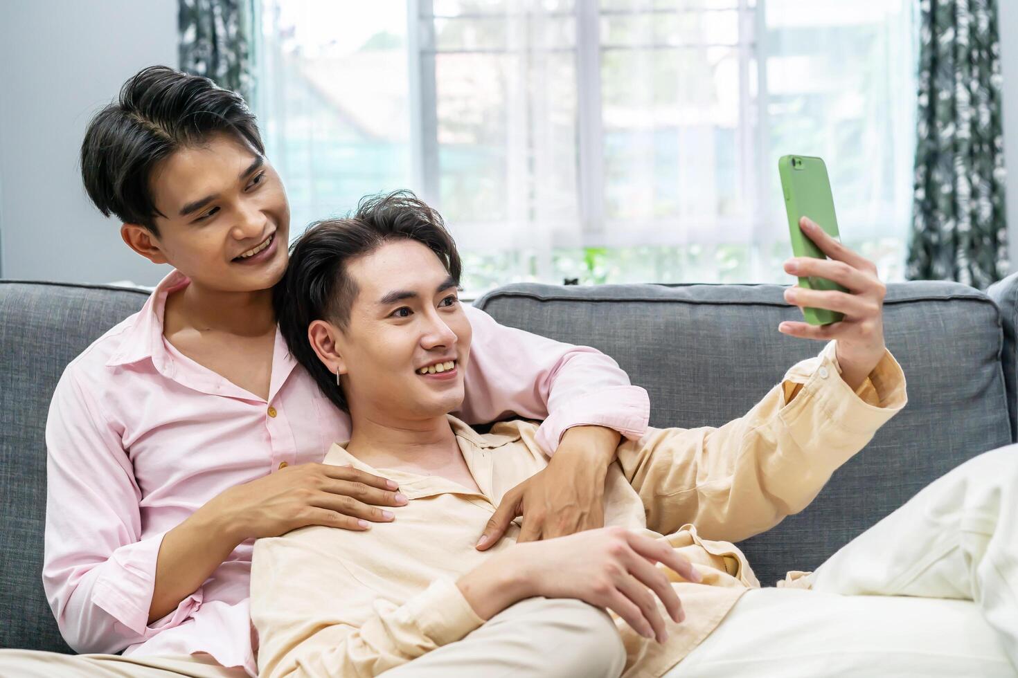 Guys Smile and Laugh in Love. Cute Male Homosexual Gay Couple Spend Time Together, Men Taking Selfie on Smartphone, sitting on a sofa in sitting room, LGBTQ, LGBT Pride Month, Gay Pride Symbol photo