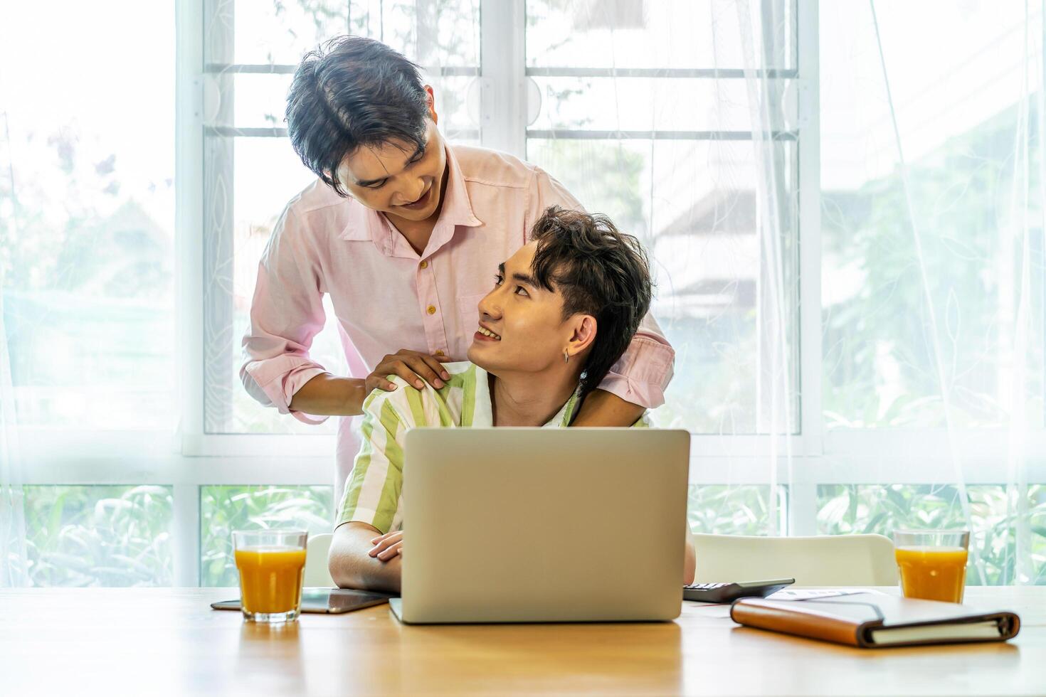 Young asian gay hugging and takes care of his boyfriend while working on his laptop at home, lgbt couple photo