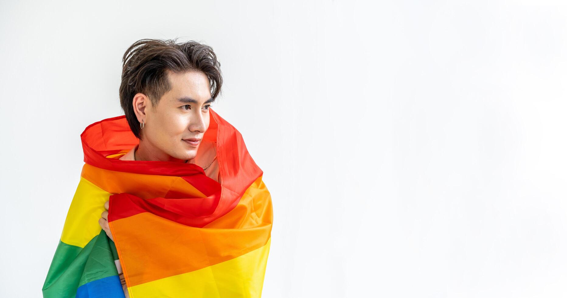 Portrait of transgender or gay man smiling in front of camera taking cover with lgbt flag on white background with copy space. People lifestyle fashion lgbtq concept photo