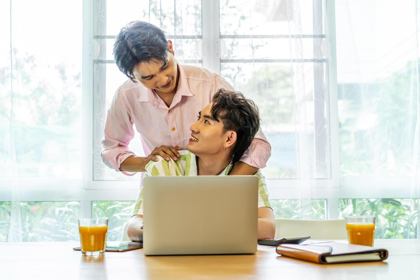 Young asian gay hugging and takes care of his boyfriend while working on his laptop at home, lgbt couple photo