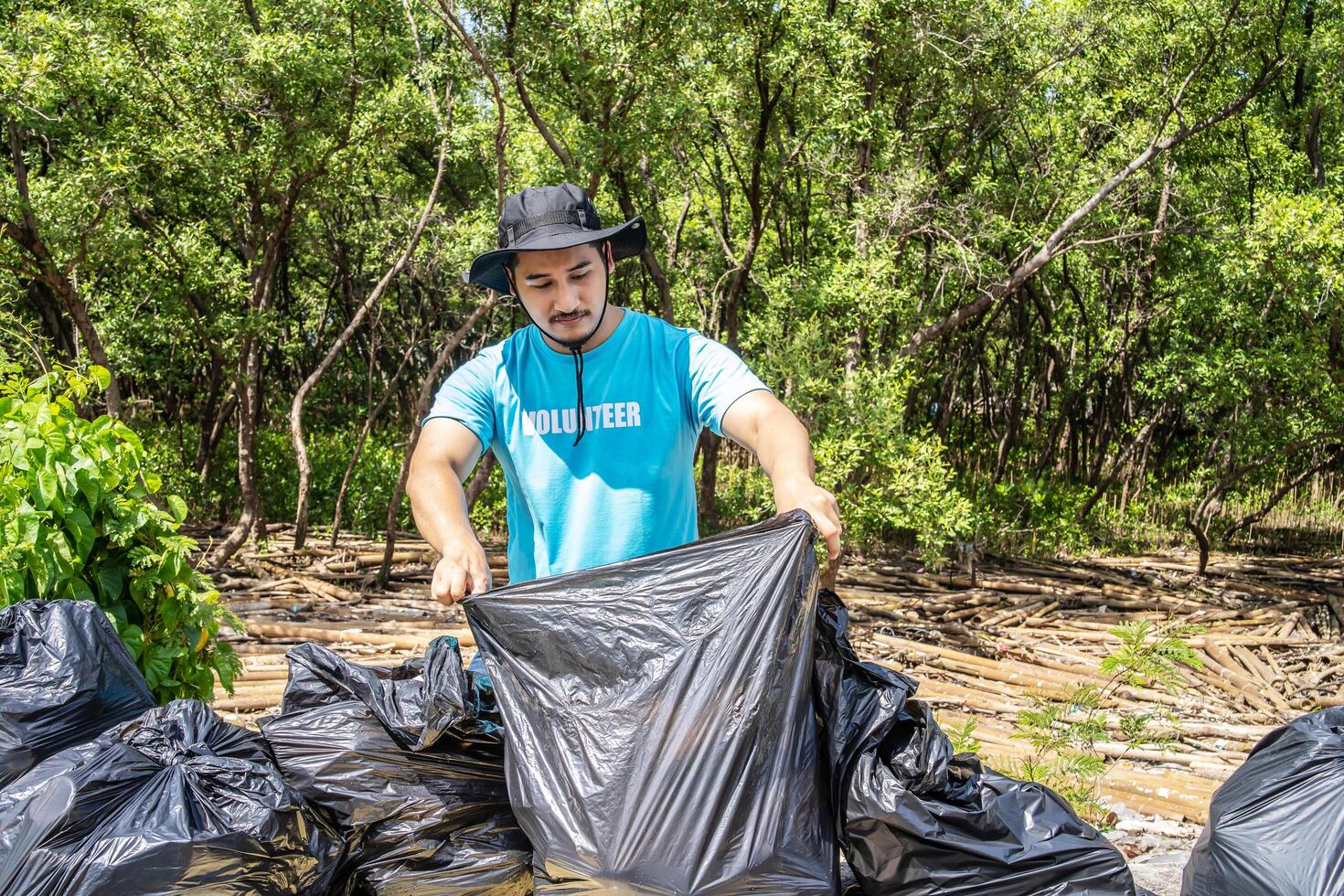 One volunteers in work overalls collect garbage in forest in plastic bag. Close-up during action. Cleaning of nature from waste. Environmental assistance. Garbage collection in forest photo