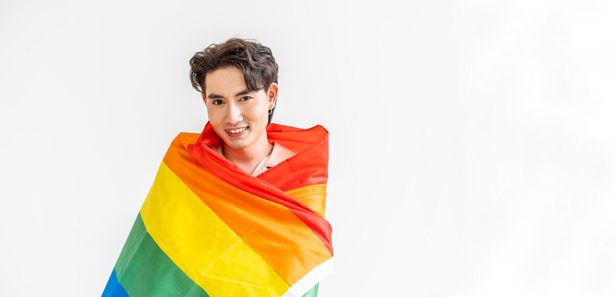 Portrait of transgender or gay man smiling in front of camera taking cover with lgbt flag on white background with copy space. People lifestyle fashion lgbtq concept photo
