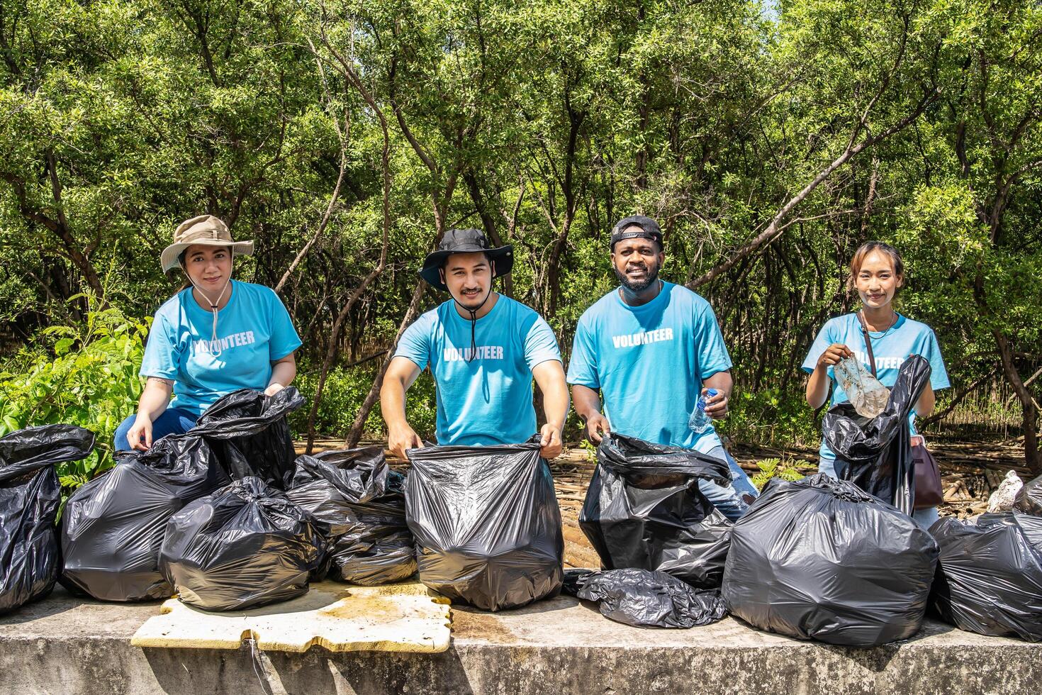 Four volunteers in work overalls collect garbage in forest in plastic bag. Close-up during action. Cleaning of nature from waste. Environmental assistance. Garbage collection in forest photo