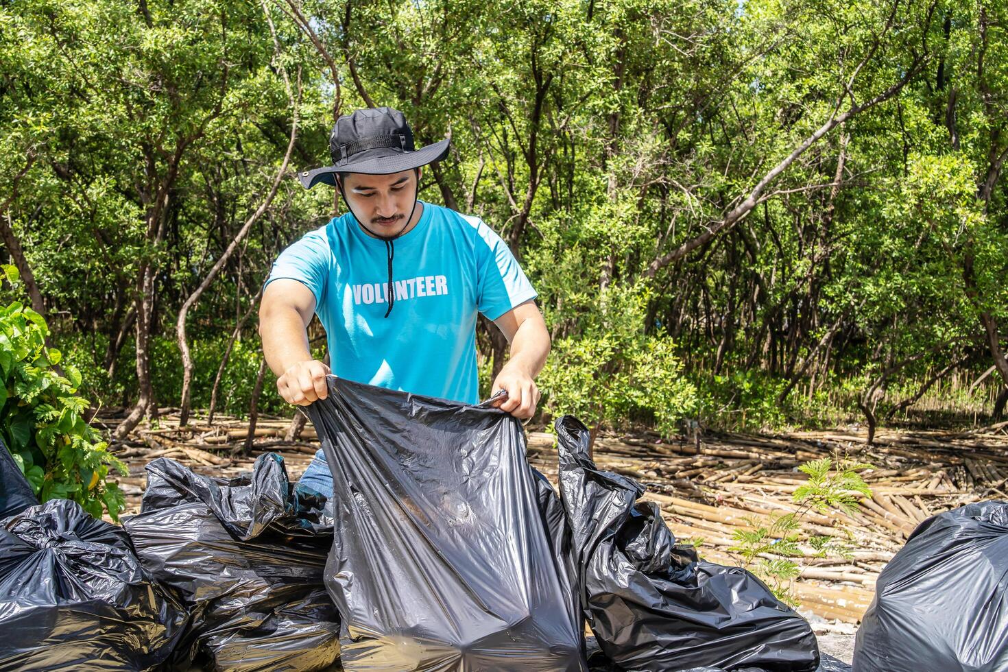 One volunteers in work overalls collect garbage in forest in plastic bag. Close-up during action. Cleaning of nature from waste. Environmental assistance. Garbage collection in forest photo