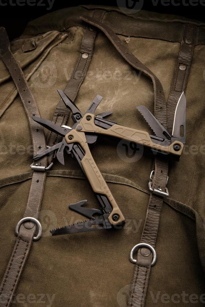 Modern multitool with many tools. A portable multitasking tool on a vintage canvas backpack. Dark back. photo