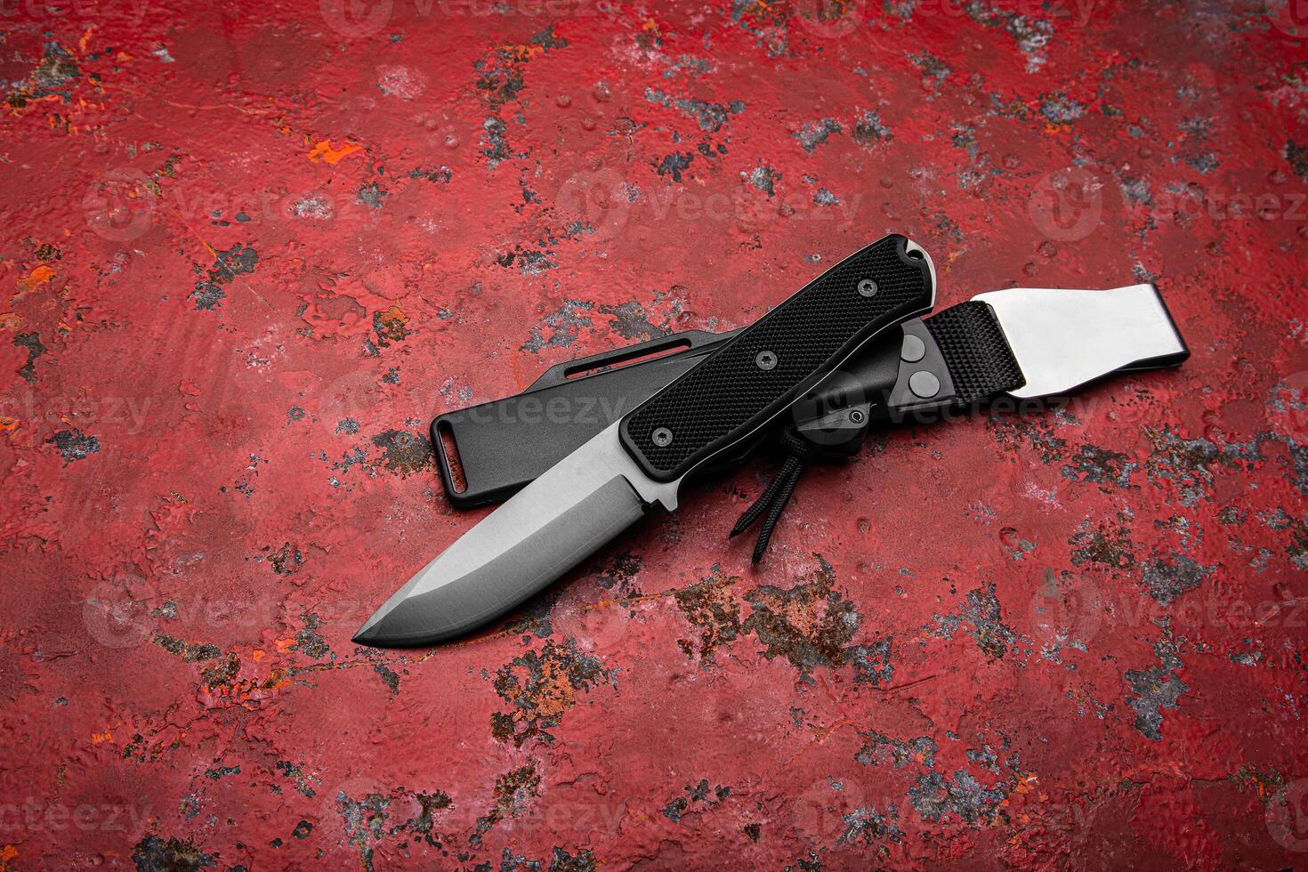 A modern hunting knife with a rubberized handle and a plastic sheath on a red back. Melee weapons for self-defense and survival. photo