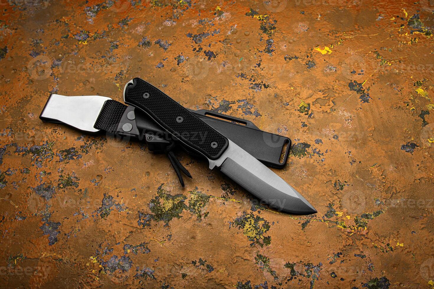 A modern hunting knife with a rubberized handle and a plastic sheath on a orange back. Melee weapons for self-defense and survival. photo