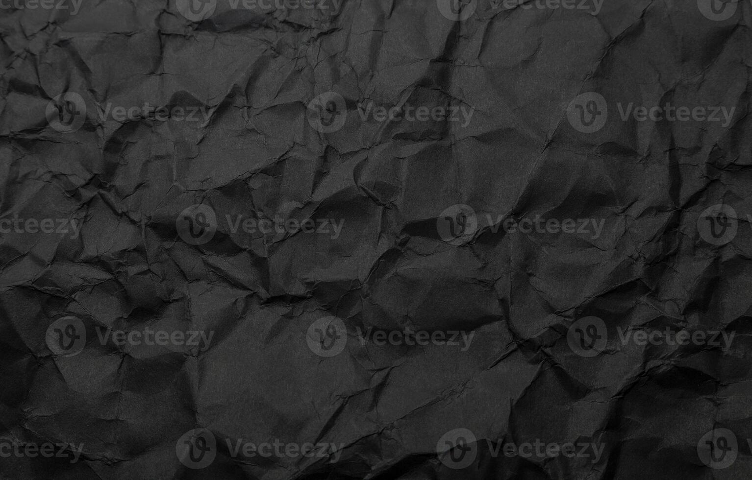 Texture of black crumpled paper. Dark paper background with chaotic bends. A sheet of black wrinkled paper photo