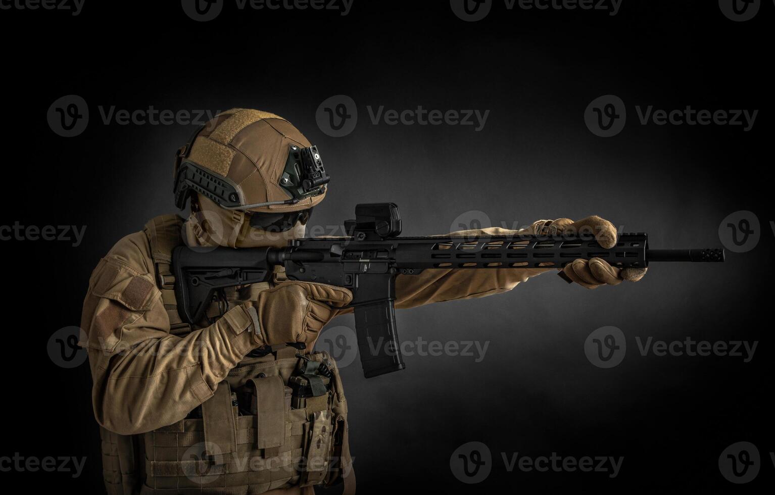 Modern soldier in full ammunition with weapons in his hands on a black background. The military aims from an automatic rifle. photo