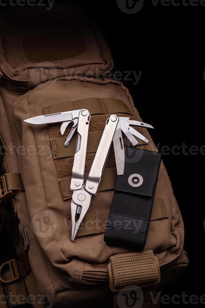 Modern multitool with many tools. A portable multitasking tool lie on a desert-colored military backpack. photo