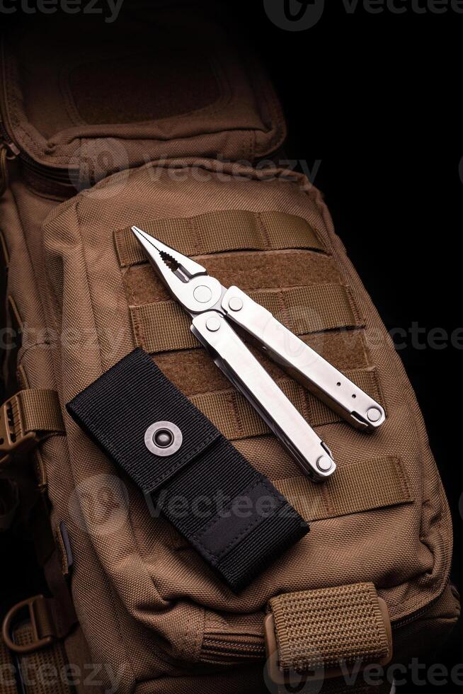 Modern multitool with many tools. A portable multitasking tool lie on a desert-colored military backpack. photo