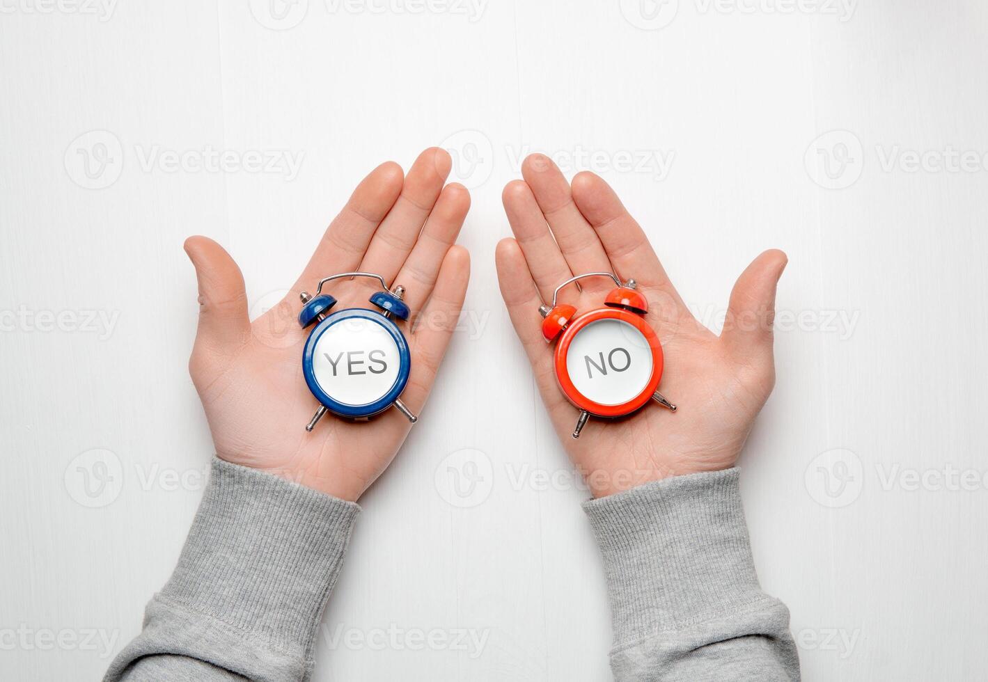 men's hands hold a red and blue alarm clock with the words yes and no. concept of choice and decision making photo