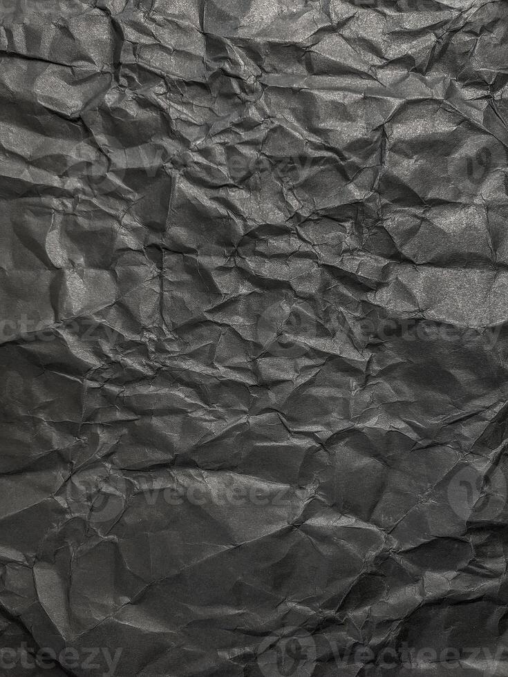Texture of black crumpled paper. Dark paper background with chaotic bends. A sheet of black wrinkled paper photo