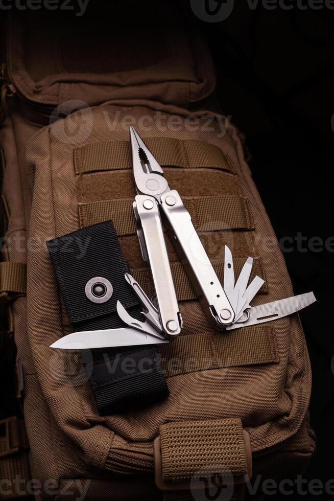 Modern multitool with many tools. A portable multitasking tool lie on a desert-colored military backpack. photo