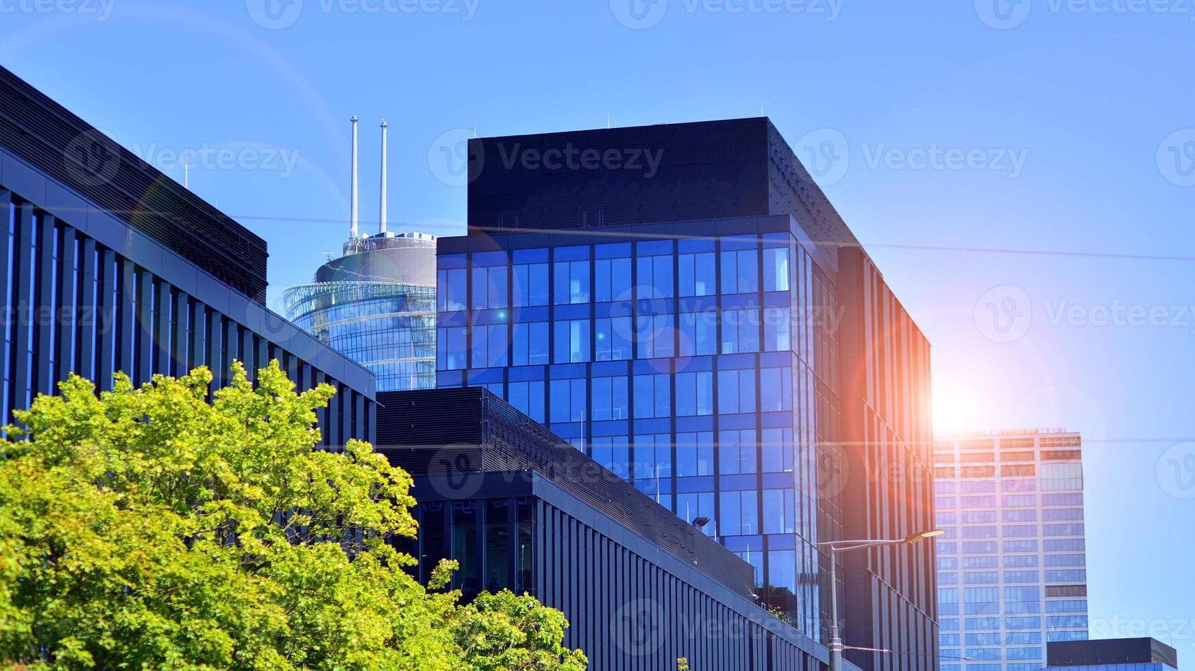 City life, urban landscape and ecology. Modern office complex with glass facades and smooth lines against backdrop of green trees, concept of modern architecture. Organically building into nature. photo