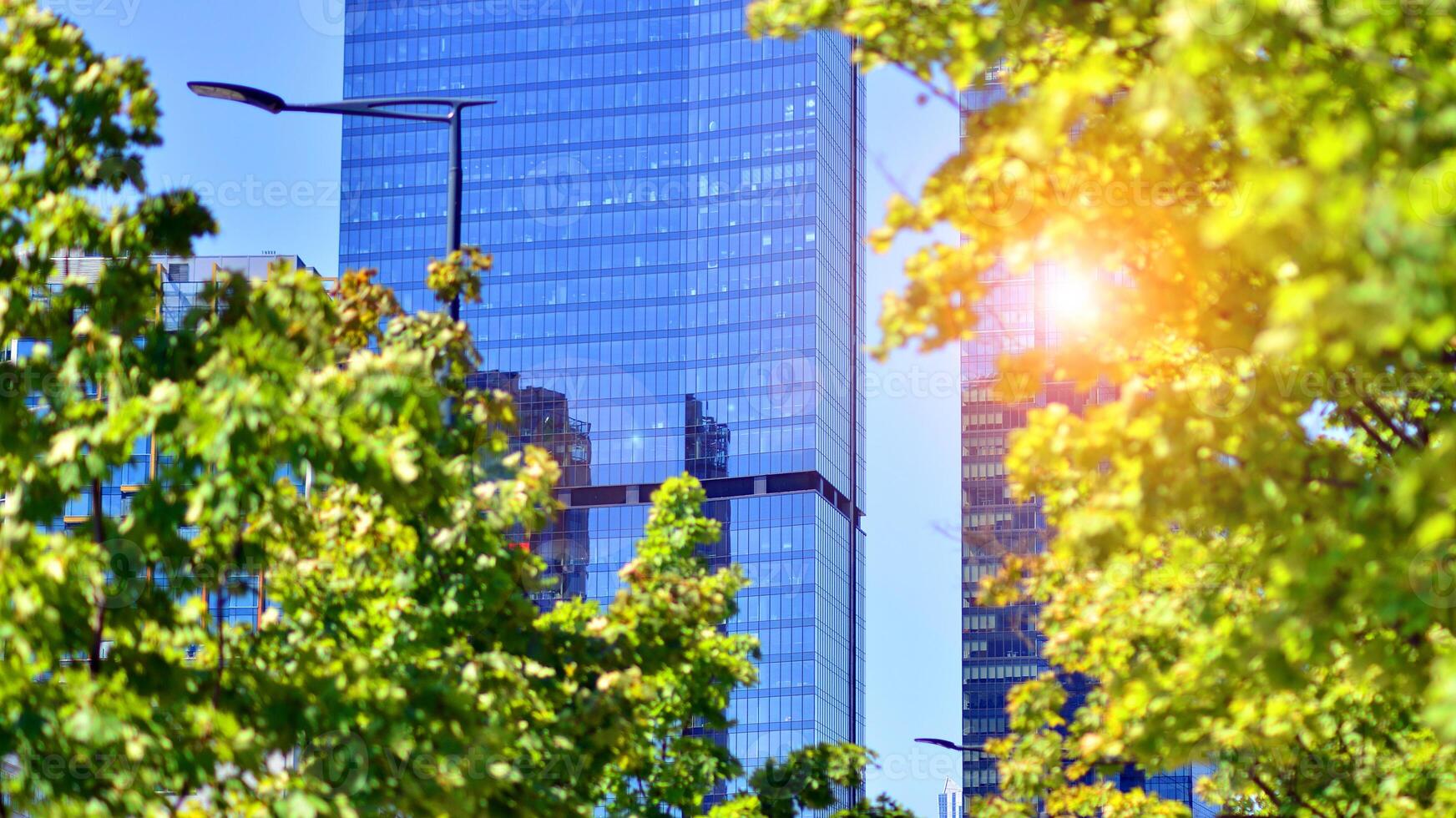 City life, urban landscape and ecology. Modern office complex with glass facades and smooth lines against backdrop of green trees, concept of modern architecture. Organically building into nature. photo