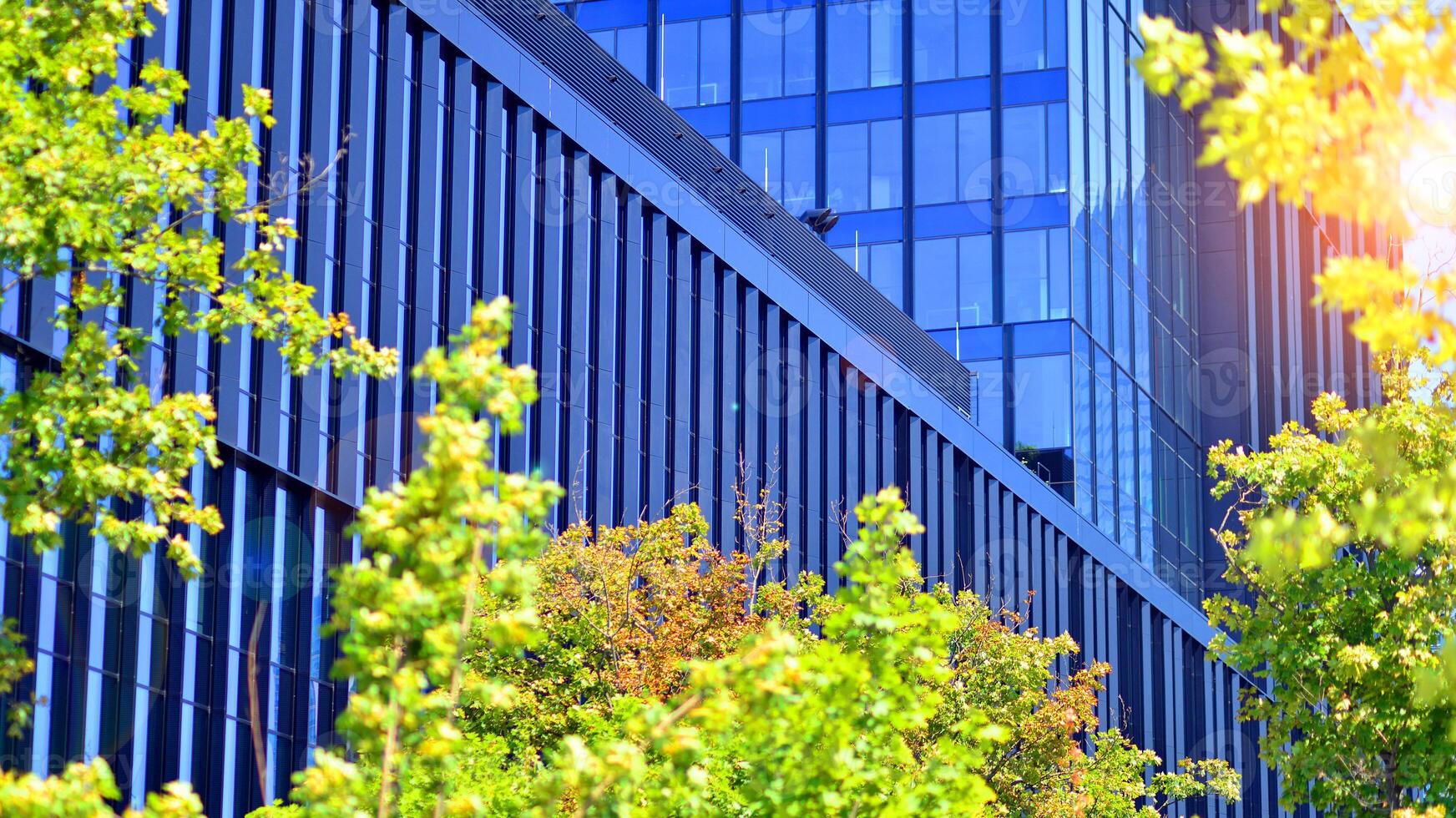 City life, urban landscape and ecology. Modern office complex with glass facades and smooth lines against backdrop of green trees, concept of modern architecture. Organically building into nature. photo