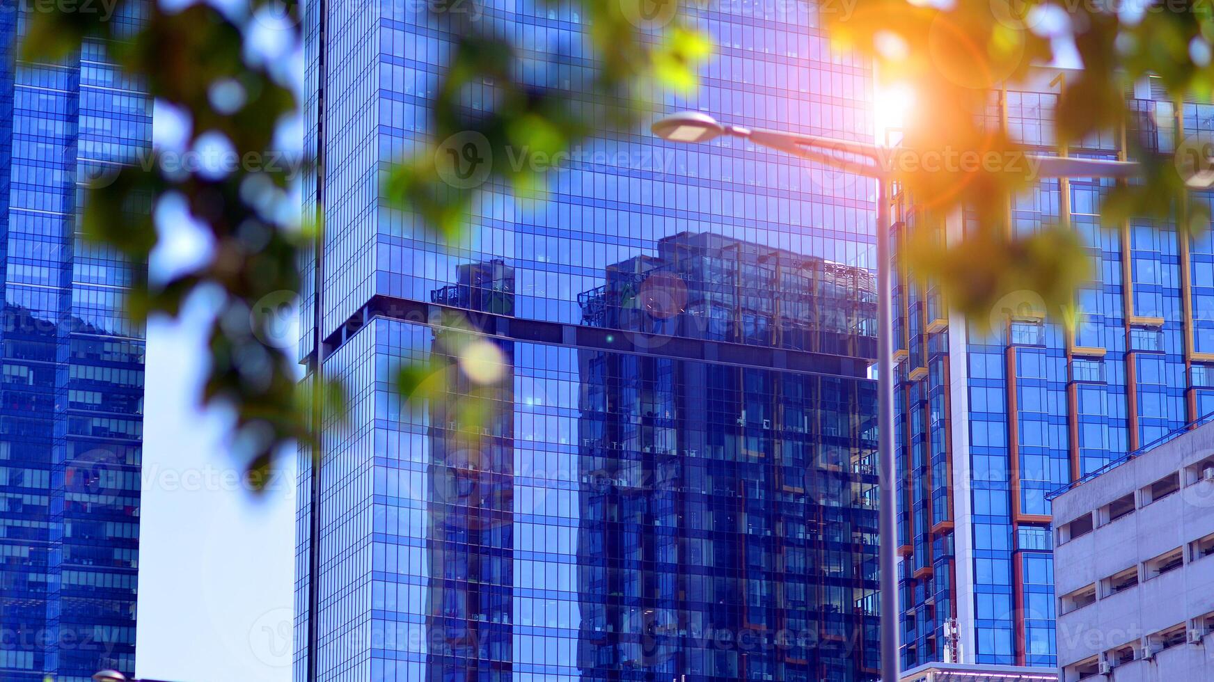City life, urban landscape and ecology. Modern office complex with glass facades and smooth lines against backdrop of green trees, concept of modern architecture. Organically building into nature. photo