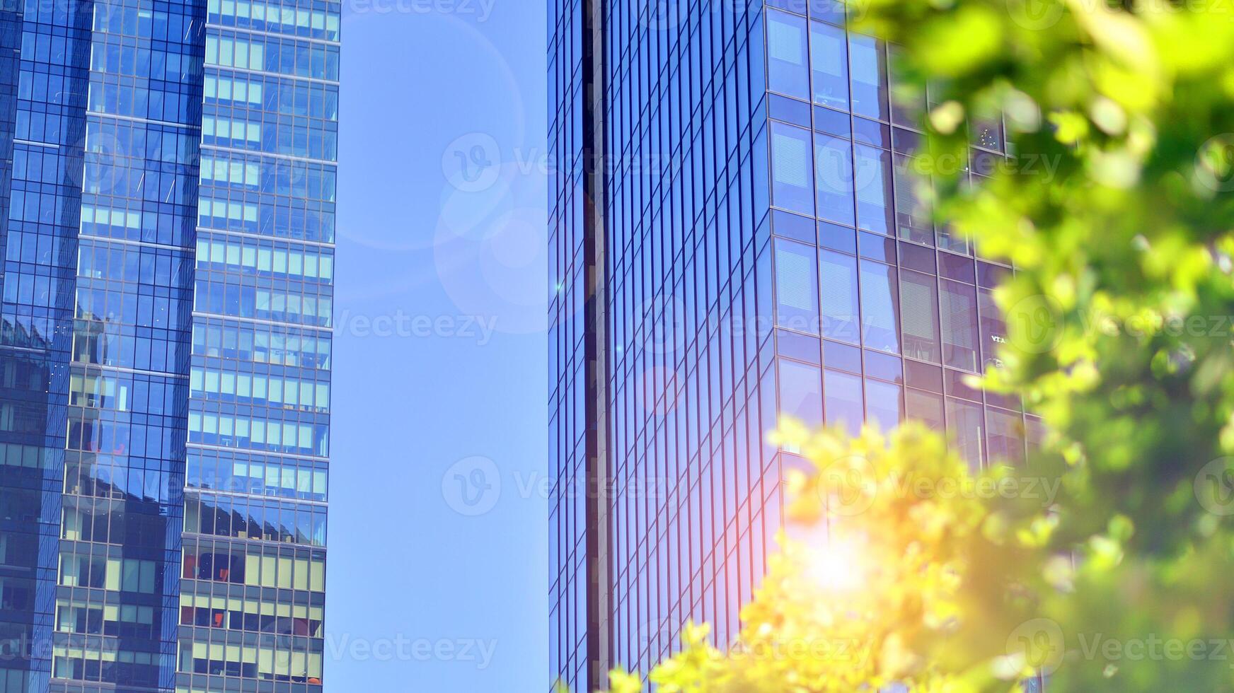 City life, urban landscape and ecology. Modern office complex with glass facades and smooth lines against backdrop of green trees, concept of modern architecture. Organically building into nature. photo