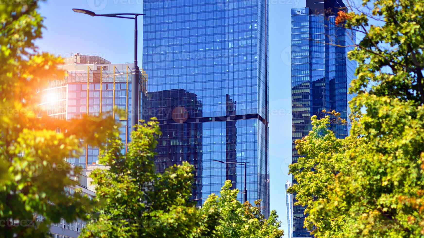 City life, urban landscape and ecology. Modern office complex with glass facades and smooth lines against backdrop of green trees, concept of modern architecture. Organically building into nature. photo