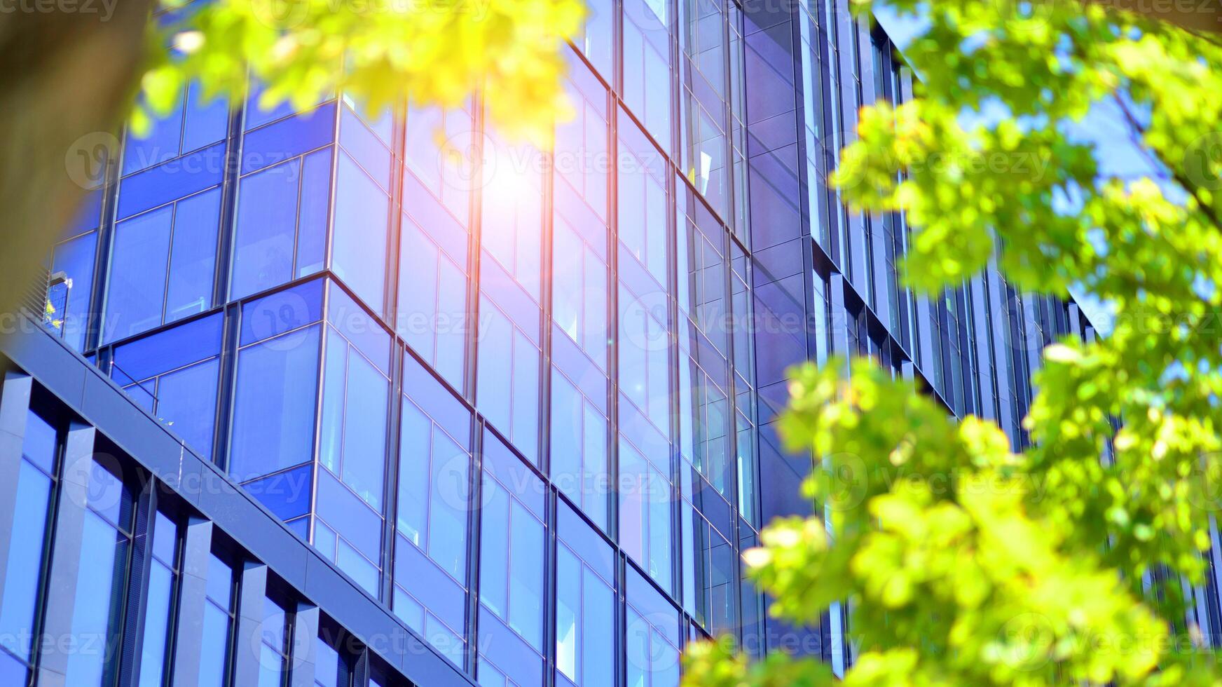 City life, urban landscape and ecology. Modern office complex with glass facades and smooth lines against backdrop of green trees, concept of modern architecture. Organically building into nature. photo
