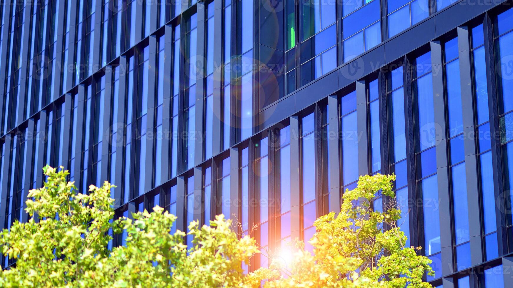 City life, urban landscape and ecology. Modern office complex with glass facades and smooth lines against backdrop of green trees, concept of modern architecture. Organically building into nature. photo
