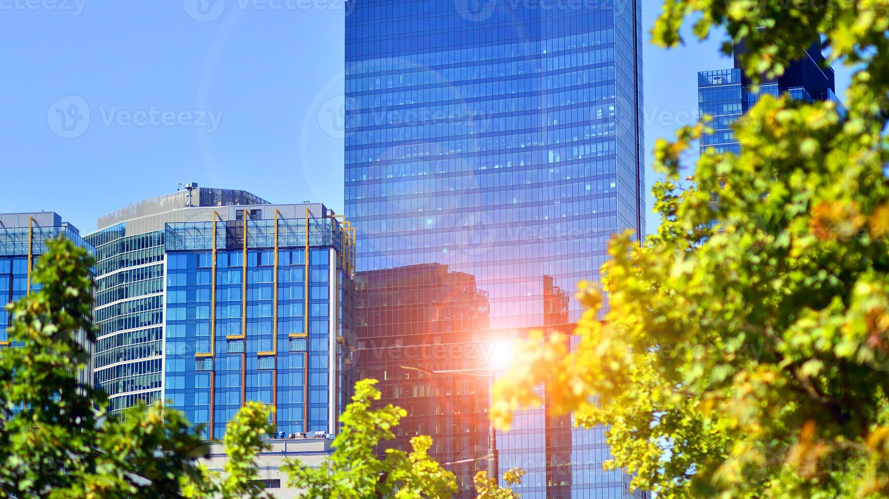 City life, urban landscape and ecology. Modern office complex with glass facades and smooth lines against backdrop of green trees, concept of modern architecture. Organically building into nature. photo
