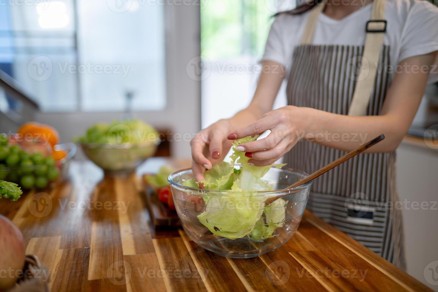 A close-up image of a woman preparing a salad bowl at the kitchen table, making healthy food at home photo