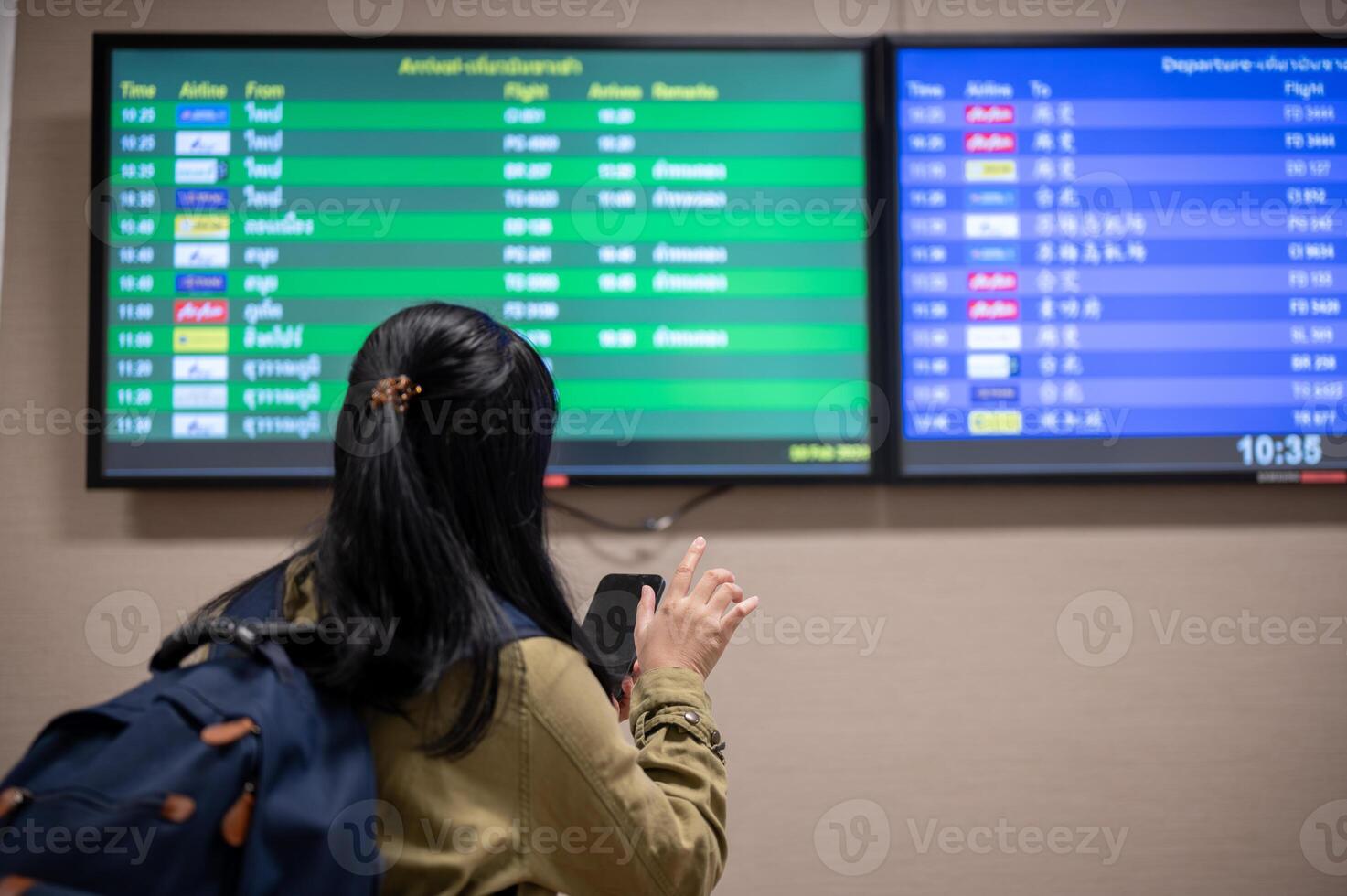 A back view shot of a female passenger checking her boarding time on a monitor screen in the airport. photo