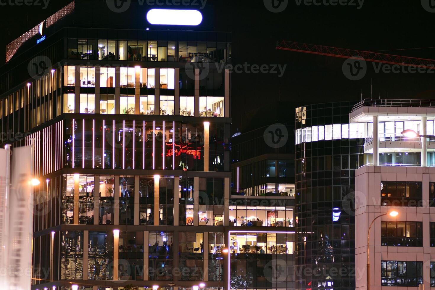 Fragment of the glass facade of a modern corporate building at night. Modern glass office in city. Big glowing windows in modern office buildings at night, in rows of windows light shines. photo