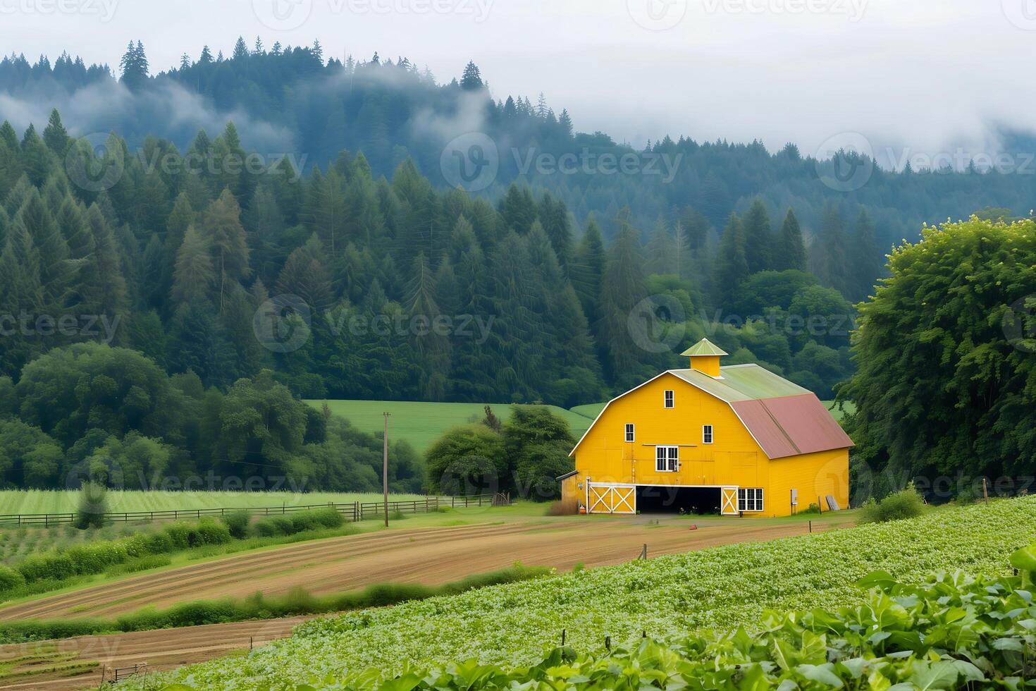 A bright yellow barn stands majestically in a verdant valley nestled amongst lush greenery and a forested hillside shrouded in mist photo