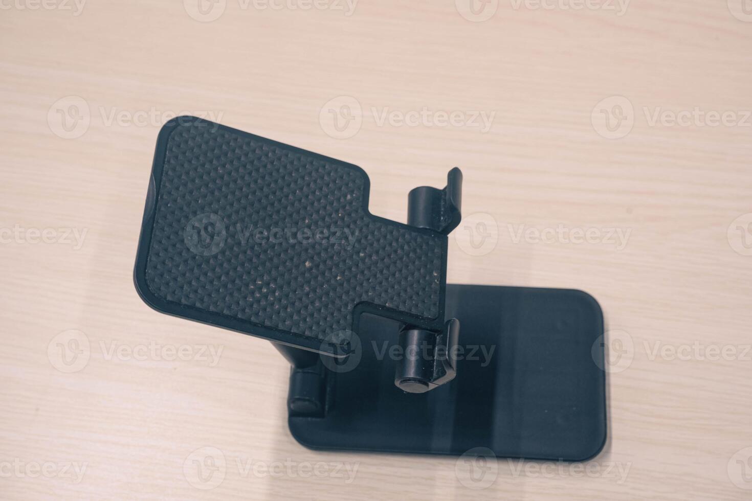 Black cell phone stand shot from the side of high engel. portable cell phone holder on wood textured background photo