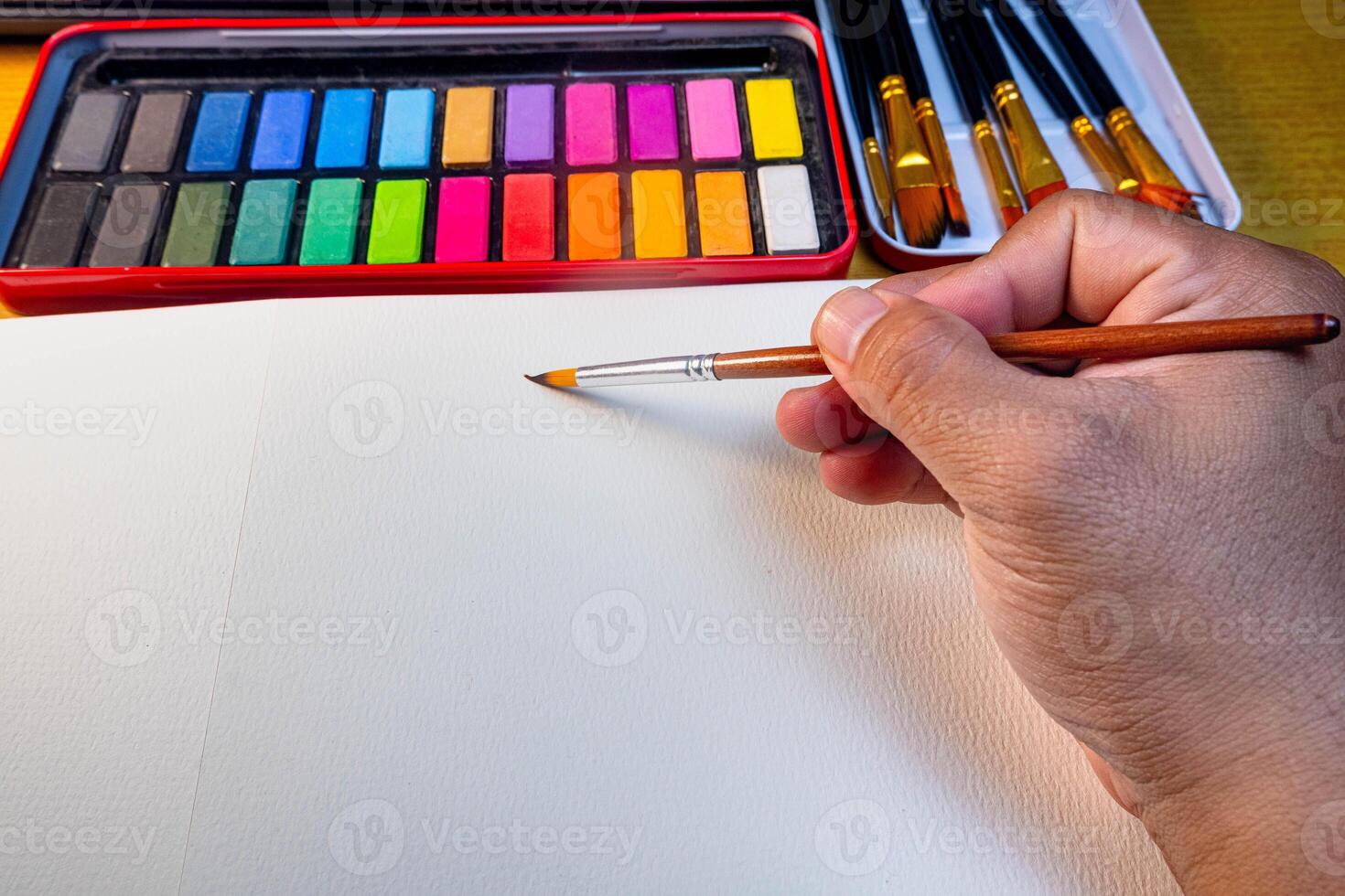 Painting in blank drawing book with brush and watercolor color palette. Paint accessories and watercolor And Blank Book on Wooden Table. Flat lay, top view. Place for text. creative concept photo
