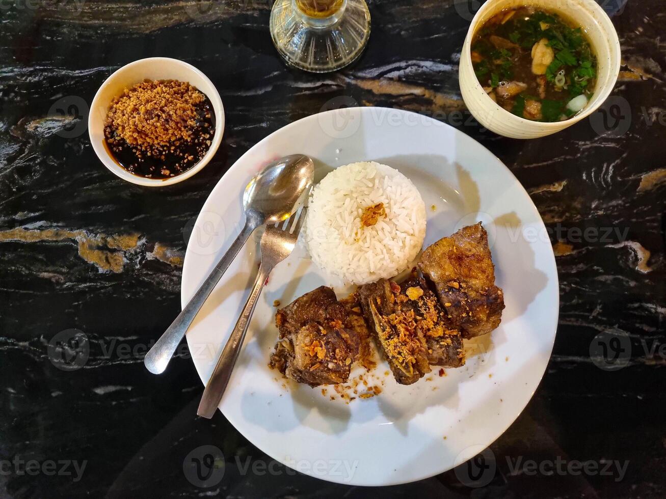 Grainy look of Iga Bakar Madu or Honey Roasted Ribs served with fried shallots on top with slice Tomatoes and a bowl of chili sauce in white background. Selective focus, Copy Space photo