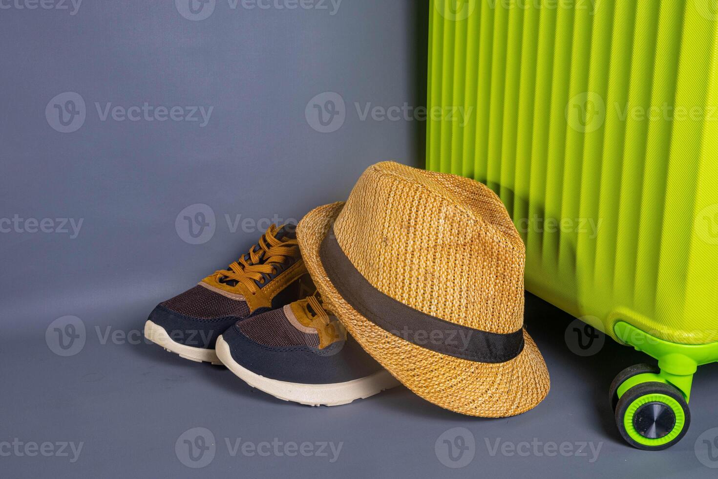 Tourist stuff. Straw hat, shoes, and green suitcase on grey background. Travel item. photo