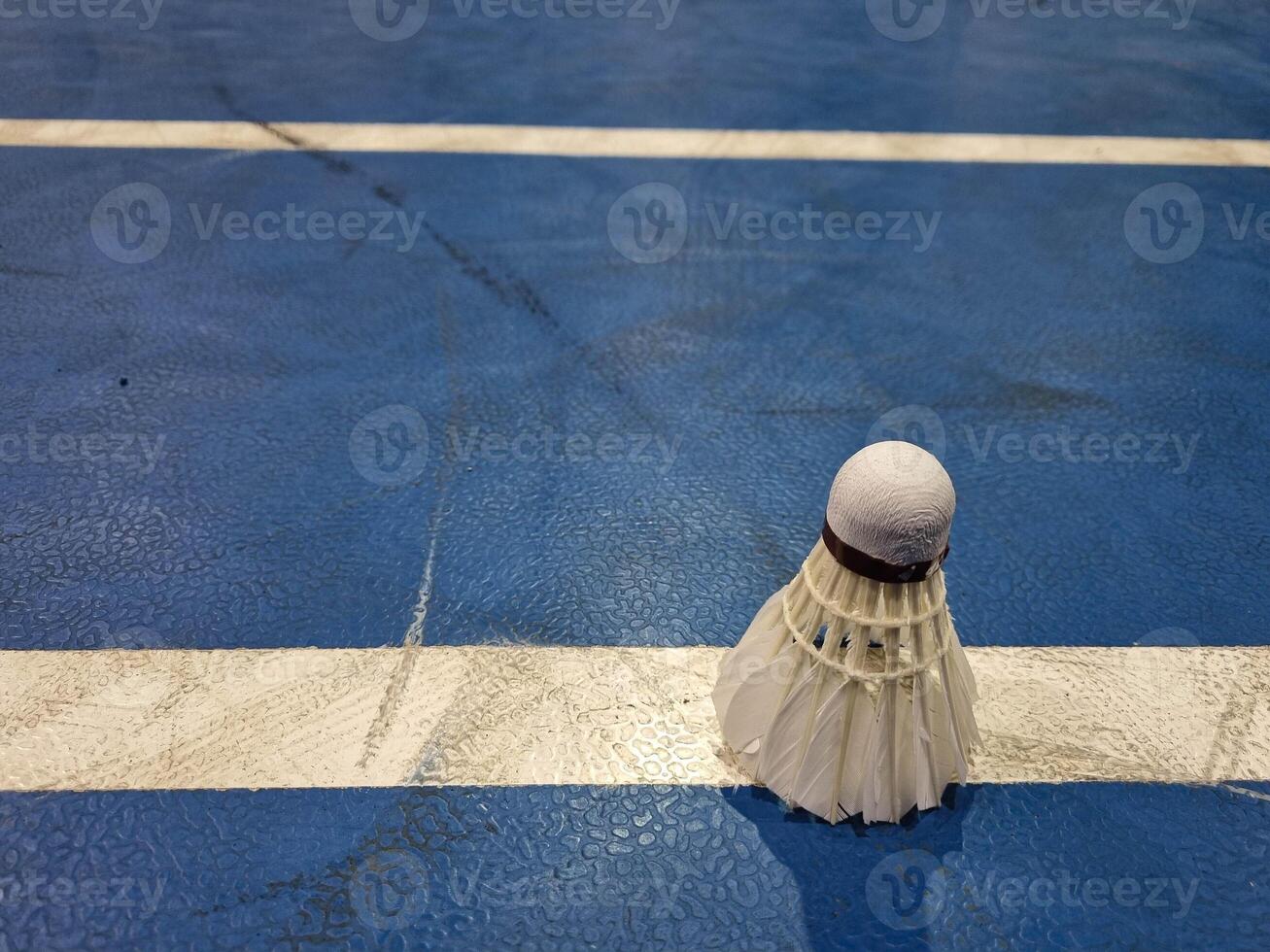 Badminton shuttlecock on blue floor in indoor badminton court, blurred badminton background, copy space photo