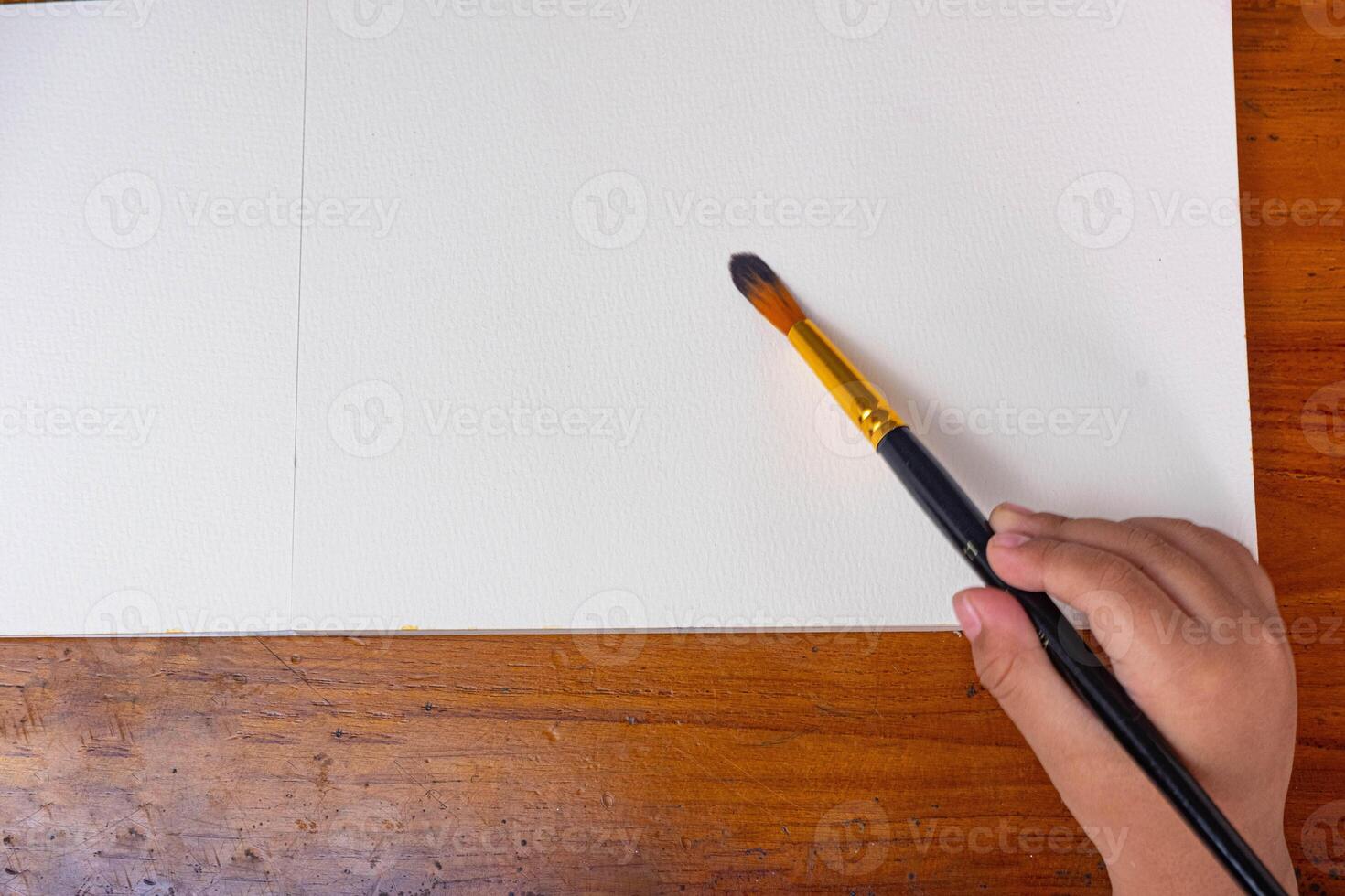 Child painting in blank drawing book with brush and watercolor color palette. Paint and watercolor accessories and Blank Books on Wooden Table. Flat lay, top view. Place for text photo