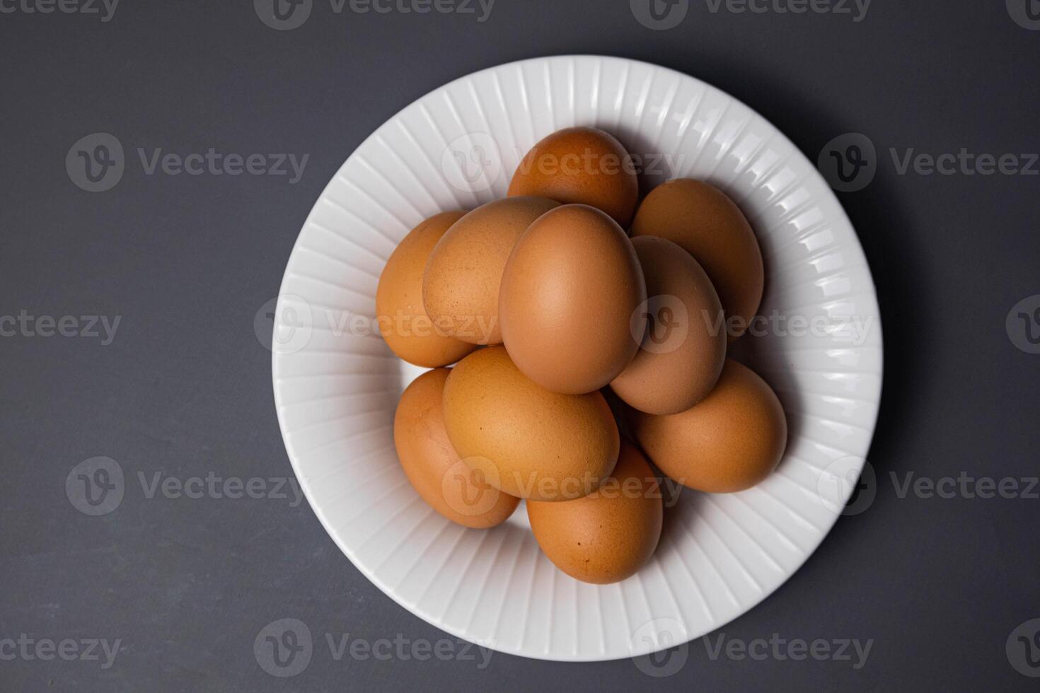 White plate with arrangement of raw chicken eggs isolated on black background. Raw chicken eggs for cooking purposes. photo