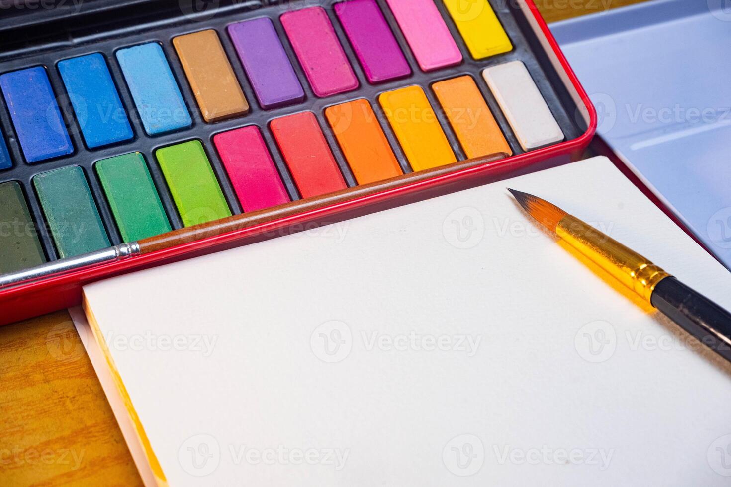 Blank drawing book and watercolor color palette. Paint accessories, watercolor and blank book on wooden table. Flat lay, top view. Place for text photo