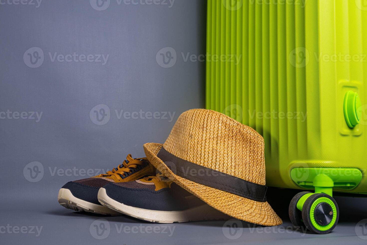 Tourist stuff. Straw hat, shoes, and green suitcase on grey background. Travel item. photo