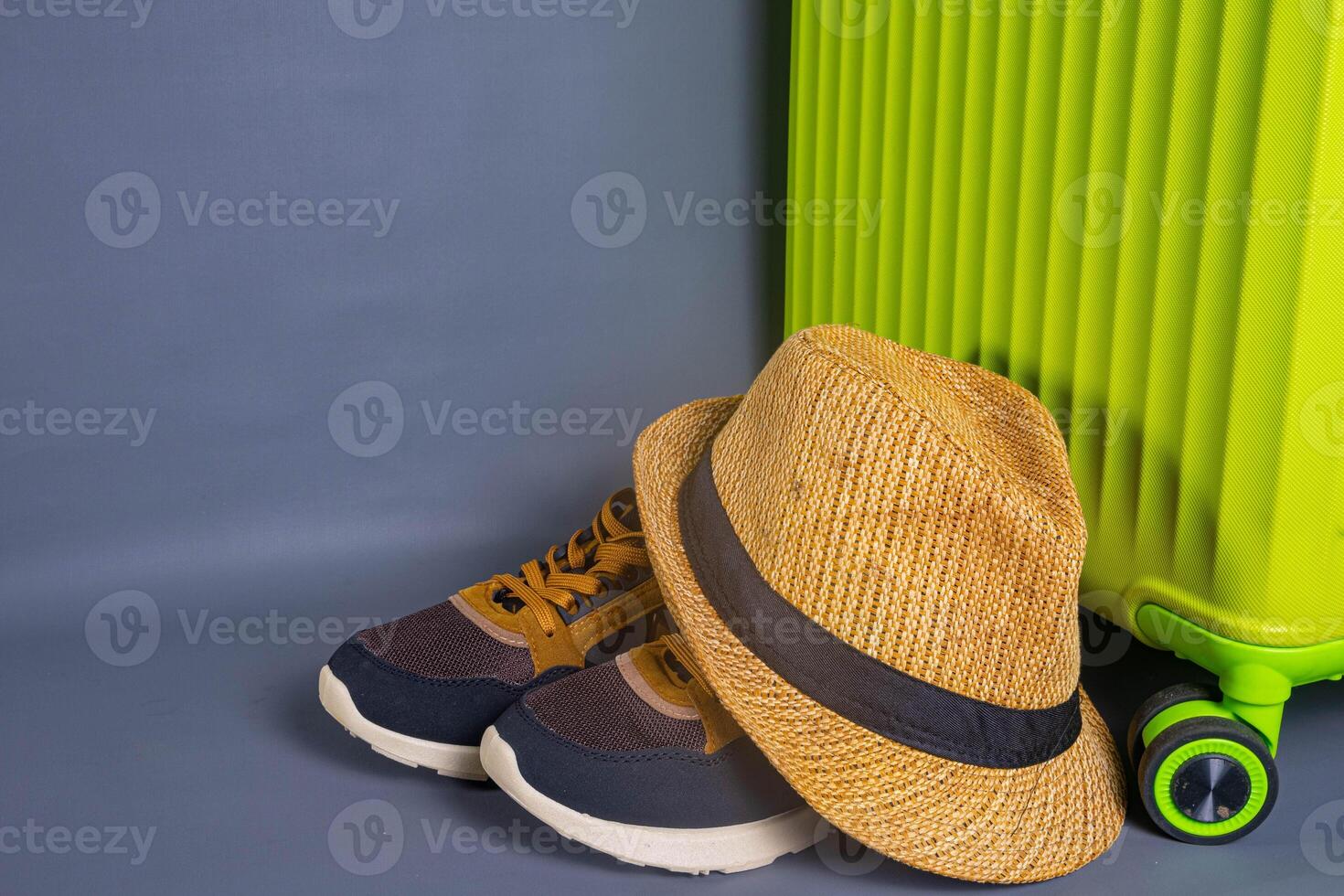 Tourist stuff. Straw hat, shoes, and green suitcase on grey background. Travel item. photo