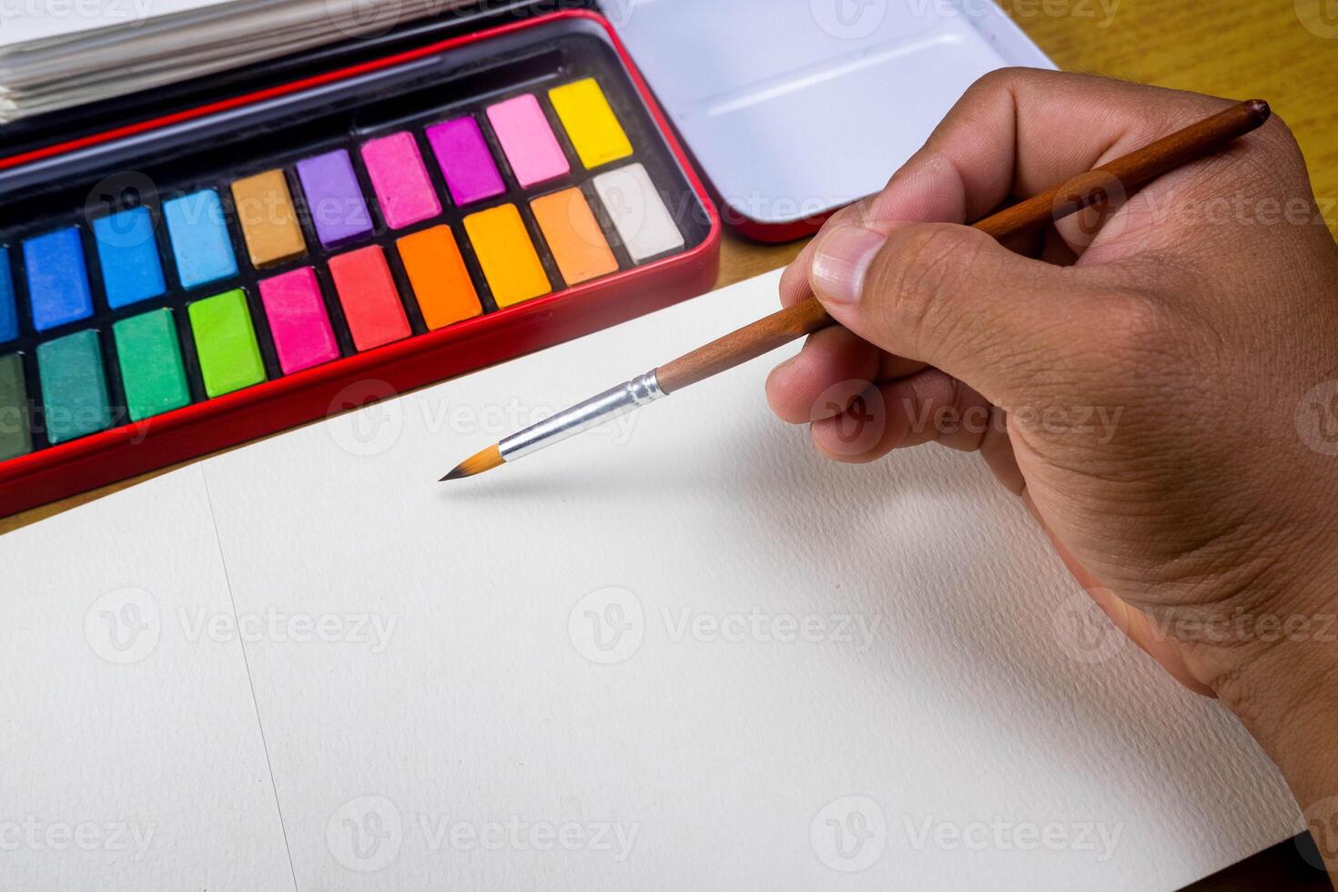 Paint accessories and watercolor and blank book on wooden table. Someone painting in blank drawing book with brush and watercolor color palette. Flat lay, top view. photo