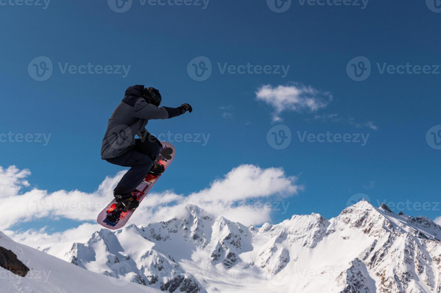 Snowboard jump in alpine landscape. Male snowboarder jumps against snowy mountains, mid-flight moment while performing trick photo